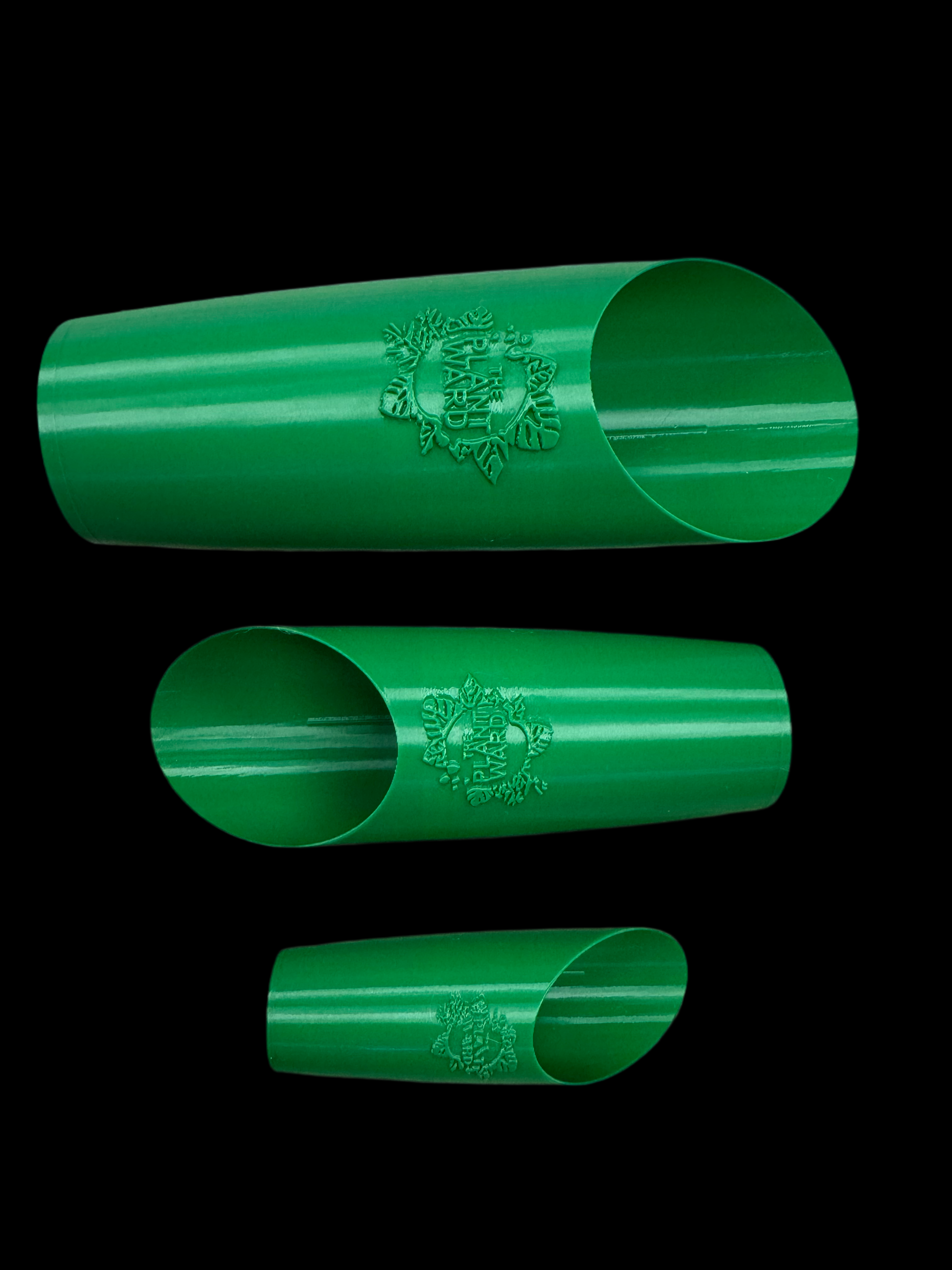 Is a photo of three green plastic soil scoops featuring the plant ward logo on front arranged smallest to largest bottom up in an alternating pattern against a black background. 